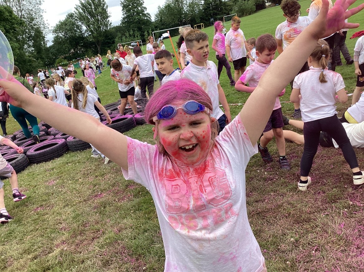 A young girl stands with her arms in the air. she is covered in pink paint.