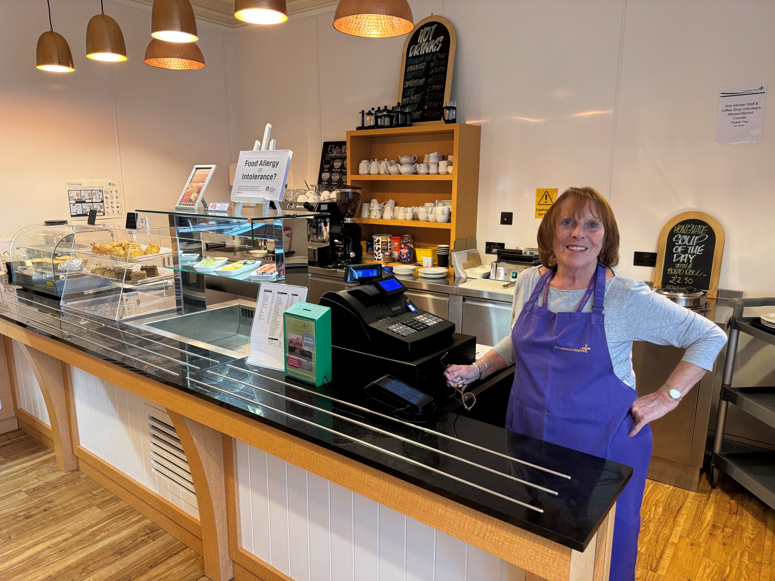 A woman with a broad smile stands behind a coffee shop counter