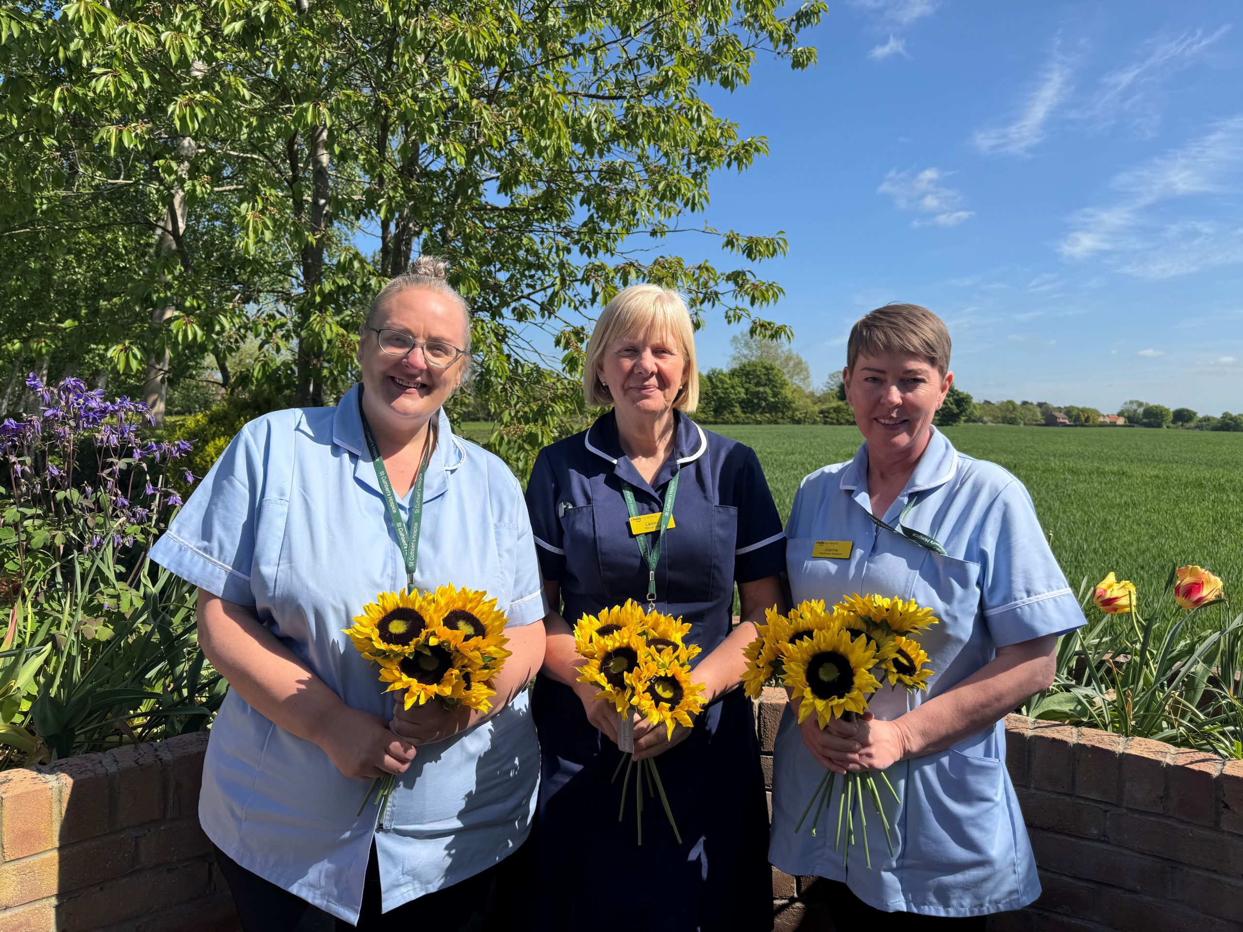 three nurses standing in the sunshine holding sunflowers