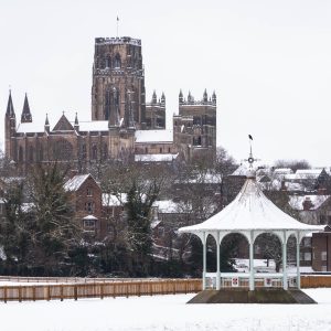 A bandstand surrounded by snow, with a Durham Cathedral rising in the background, showcasing a picturesque winter scene.