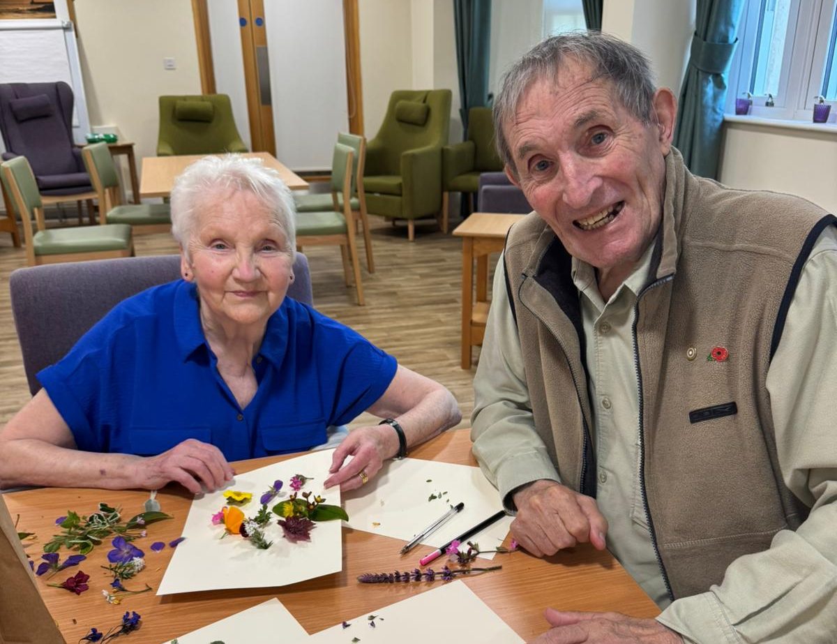 A woman and man sit at a table with flowers and paper on it.