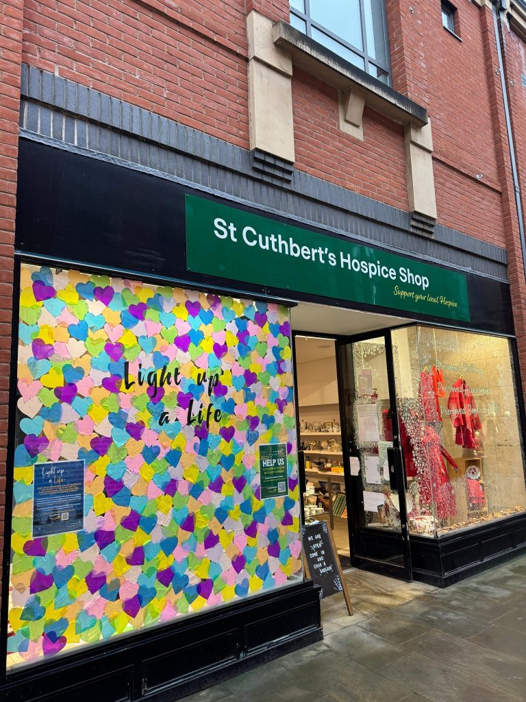 A view of St Cuthbert's Hospice shop front showing vibrant colourful window covered with hearts
