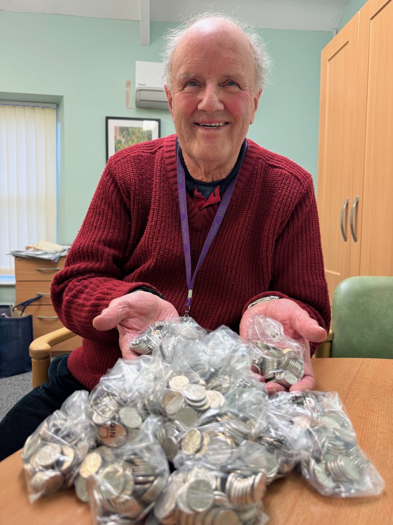 An older man smiles while holding a large pile of coins in his hands, showcasing his collection.