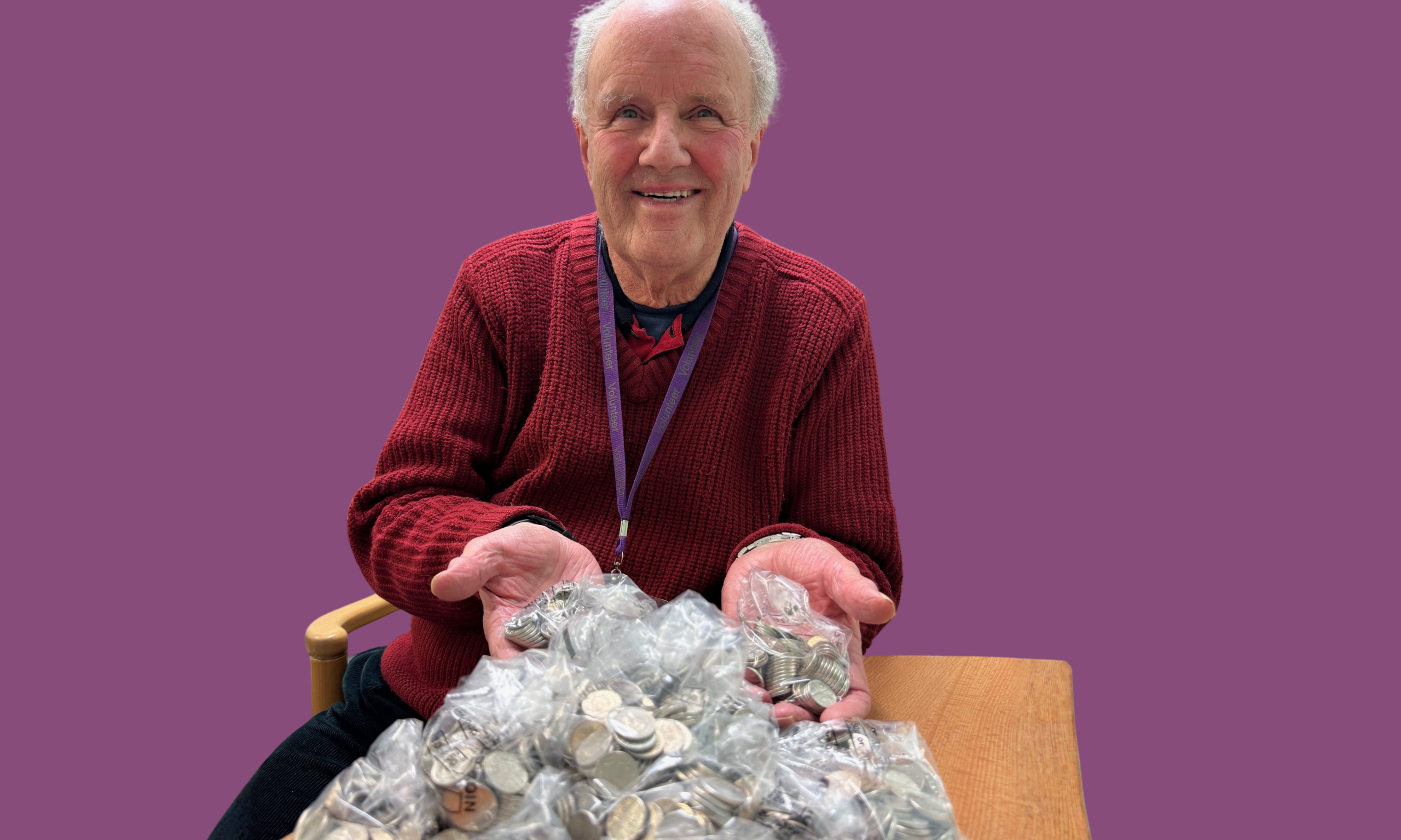 An older man smiles while holding a large pile of coins in his hands, showcasing his collection.
