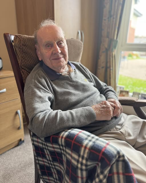 99 year old George sits in a high back chair smiling gently